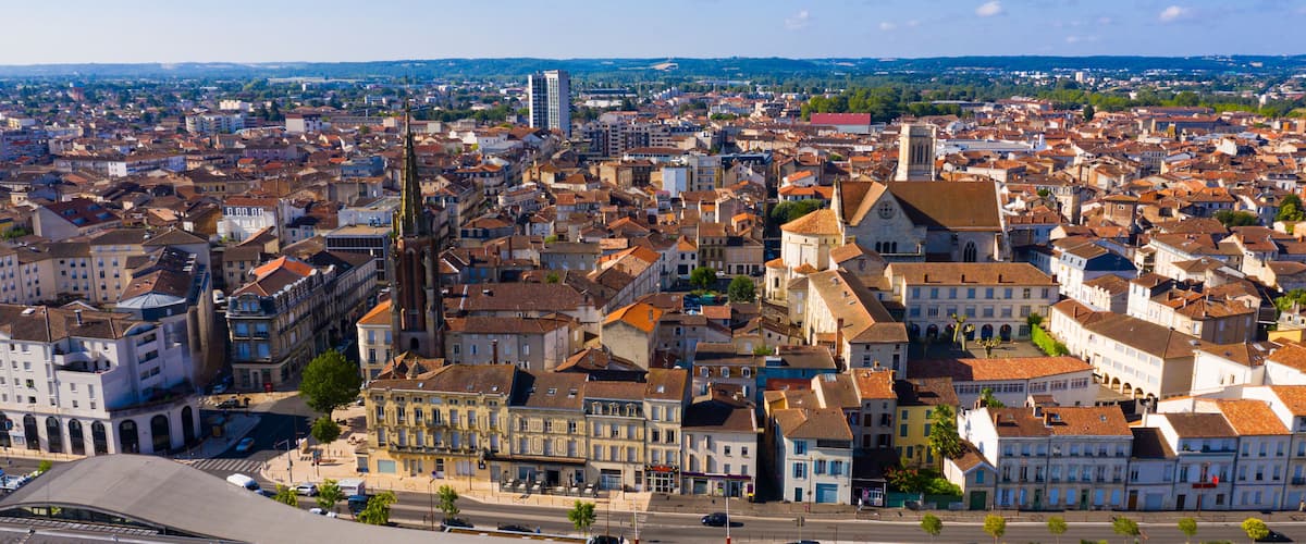 A panoramic view of a historic city with dense architecture, a prominent church tower, and a river in the distance.