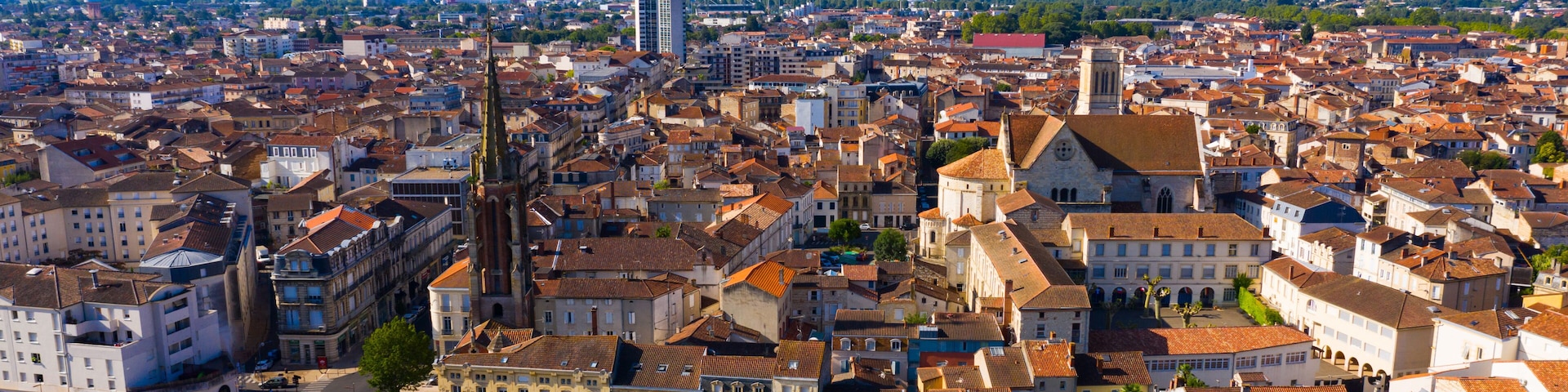 A panoramic view of a historic city with dense architecture, a prominent church tower, and a river in the distance.