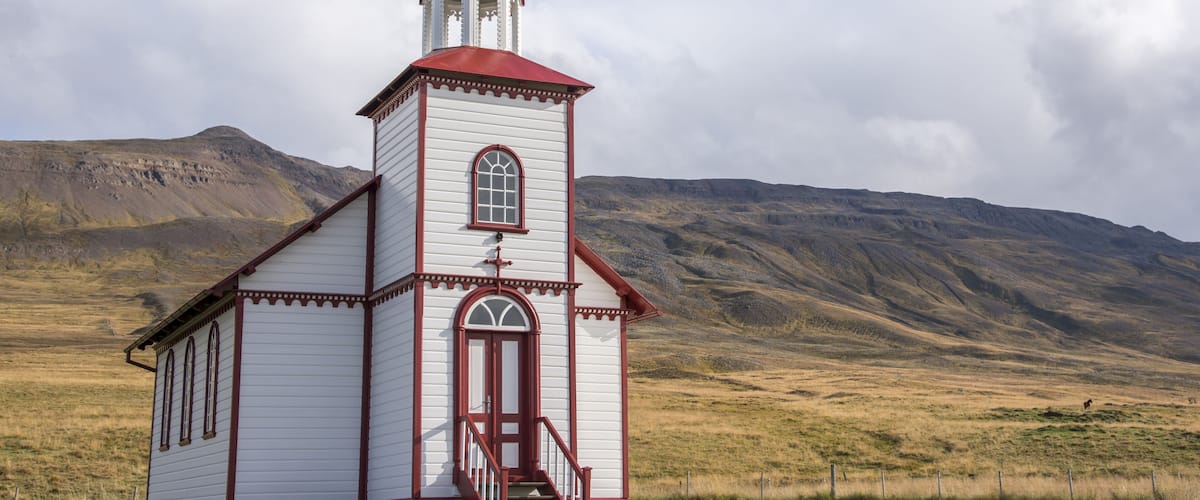 A white church with a red roof and steeple, set against a mountainous backdrop.