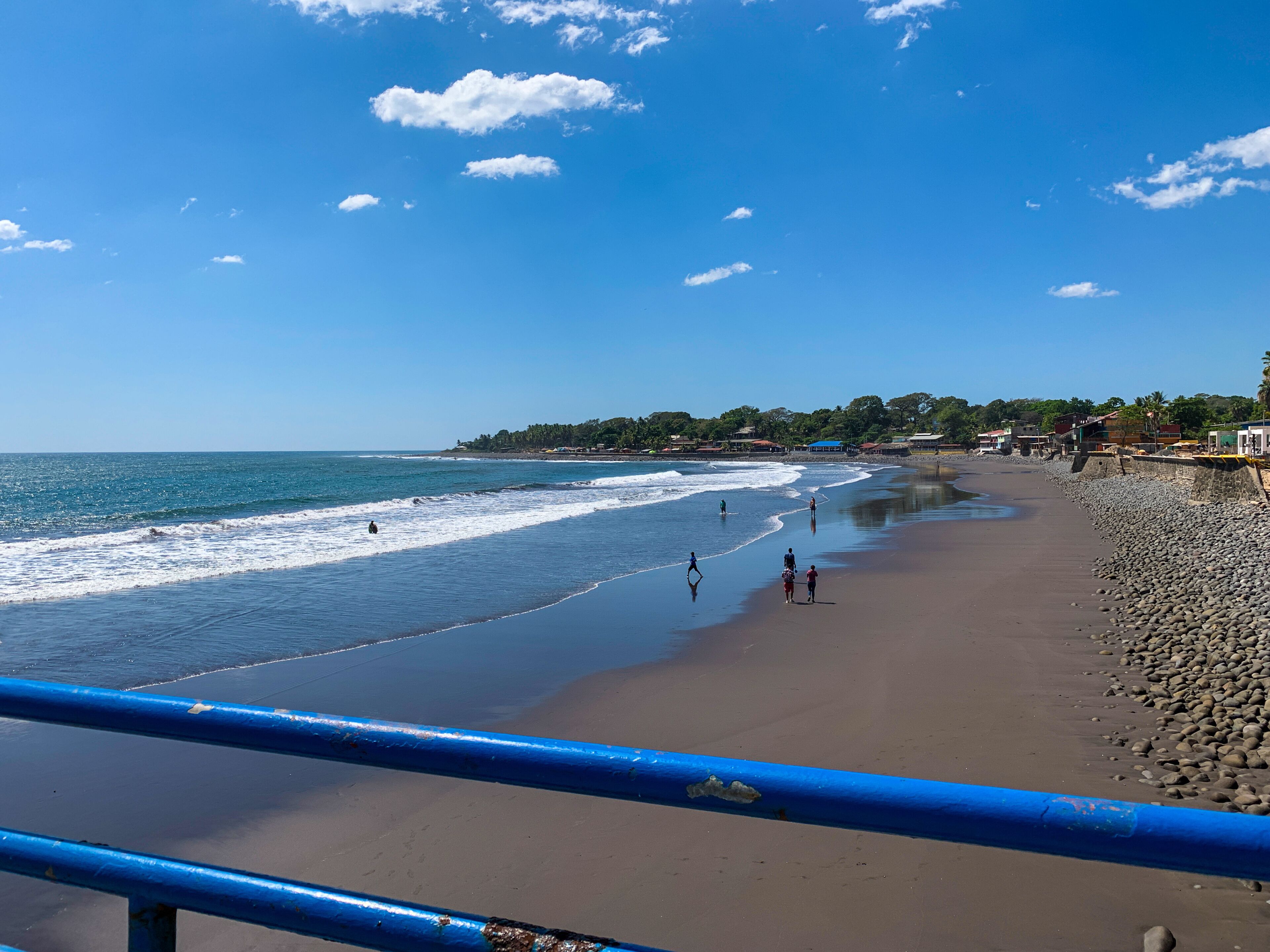 Uma praia com ondas, pessoas e céu claro.