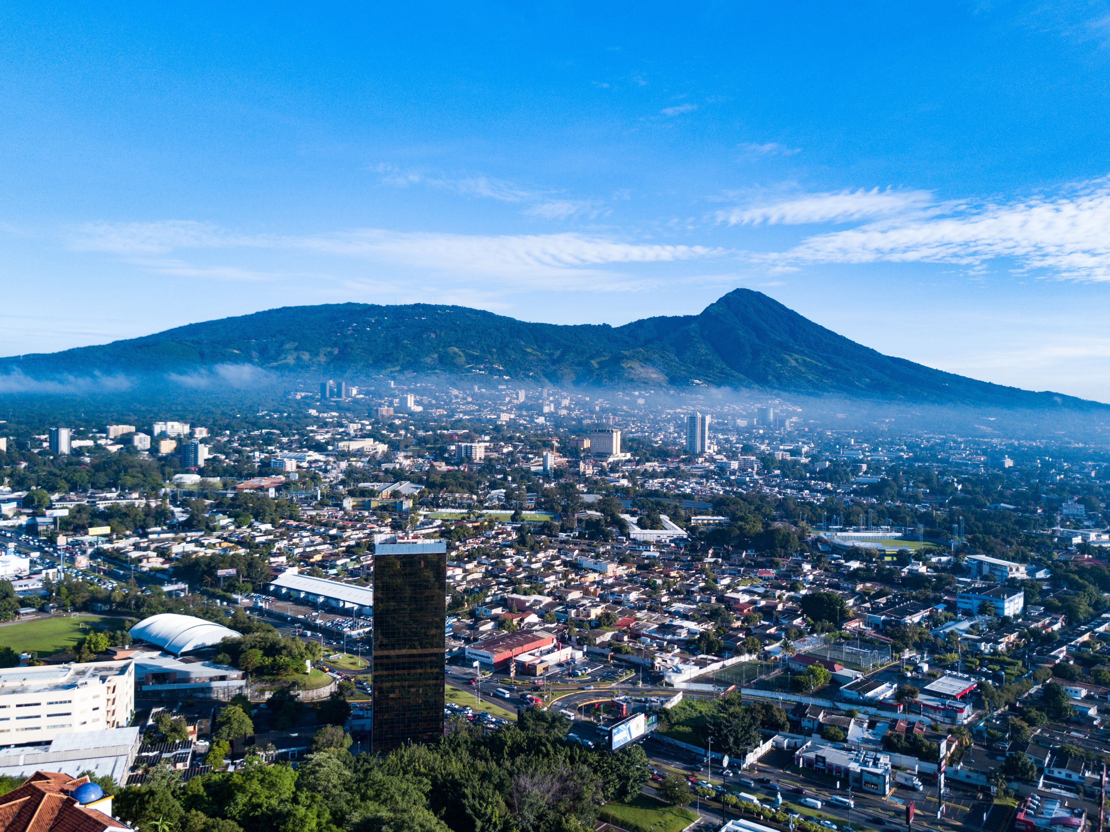 A cityscape with a prominent mountain in the background, a tall tower in the foreground, and a mix of residential and commercial buildings.