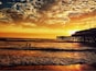 A sunset over a beach with waves and a pier.