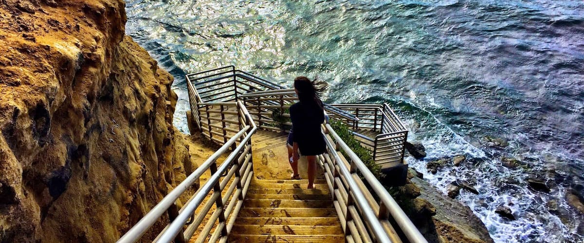 A wooden staircase leading down to a rocky shoreline with waves crashing below.