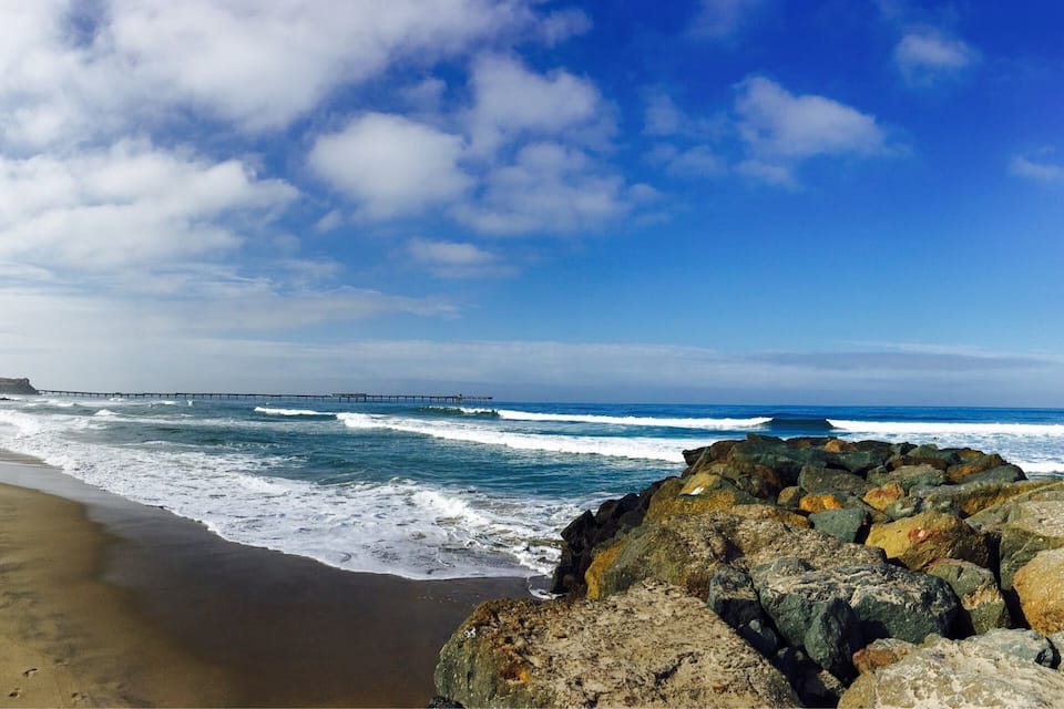 Uma praia com ondas, um cais e um litoral rochoso.