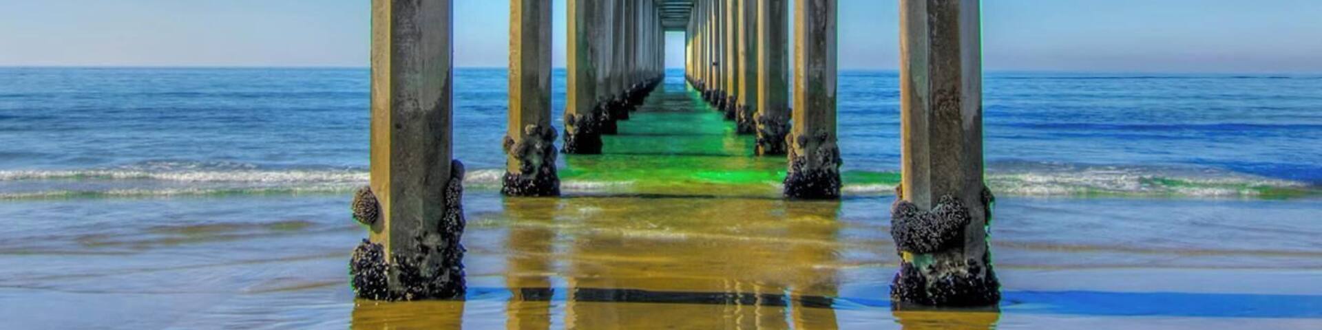 A pier extending into the ocean with clear blue water and a sandy beach.