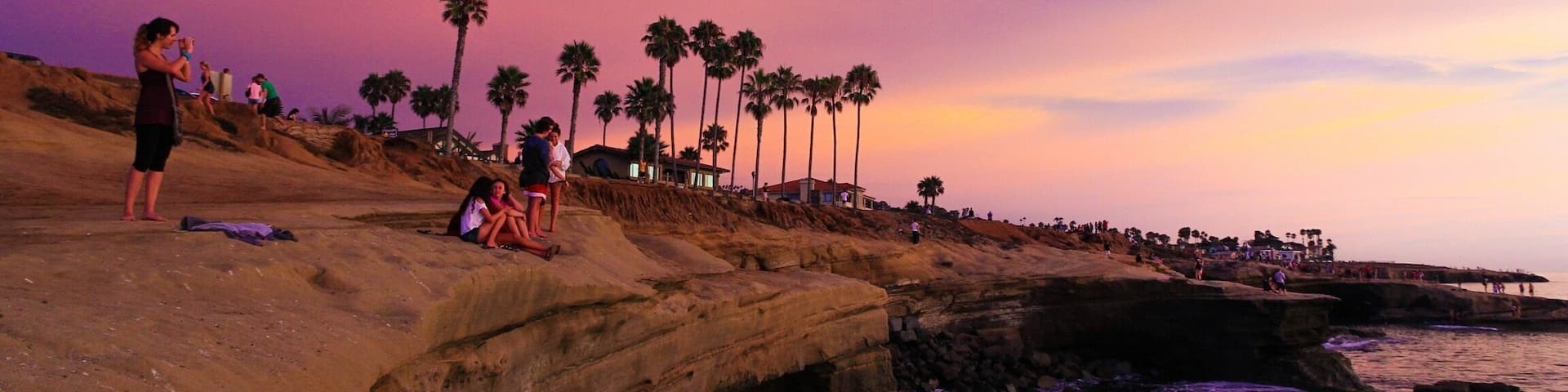 A rocky coastline with palm trees and people at sunset.