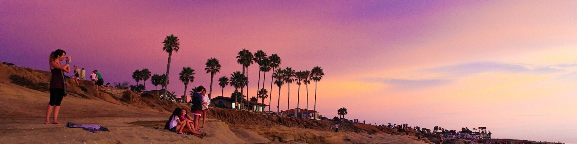 Costa rocosa con palmeras y gente al atardecer.