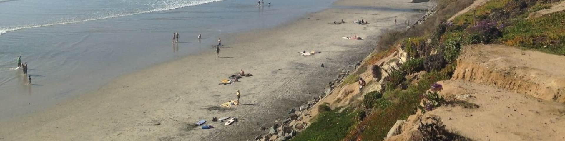 A coastal beach with people walking and swimming, sandy dunes, and ocean waves.