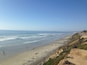 Une plage côtière où l’on peut voir des gens se promener et nager, des dunes de sable et des vagues de l’océan.