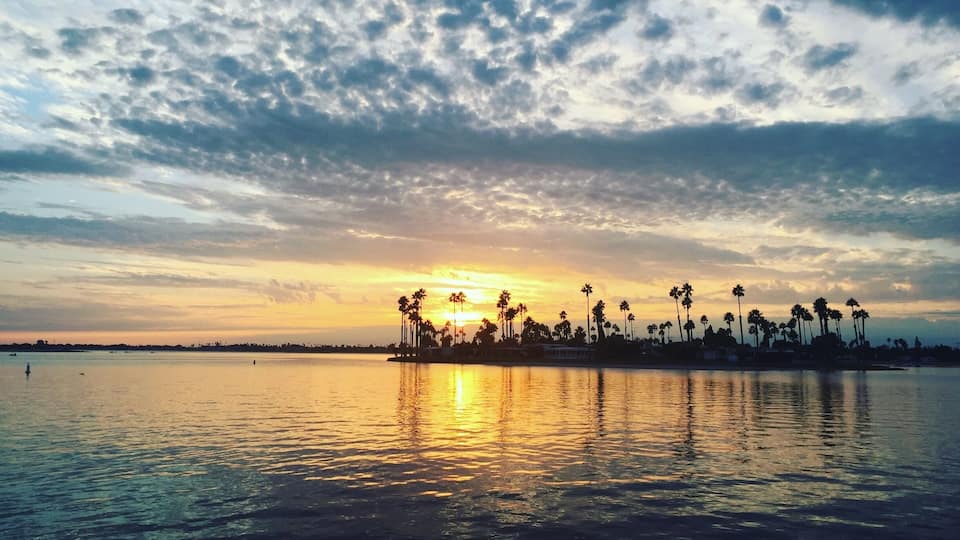 Um pôr do sol sobre águas calmas, com palmeiras em silhueta no céu.