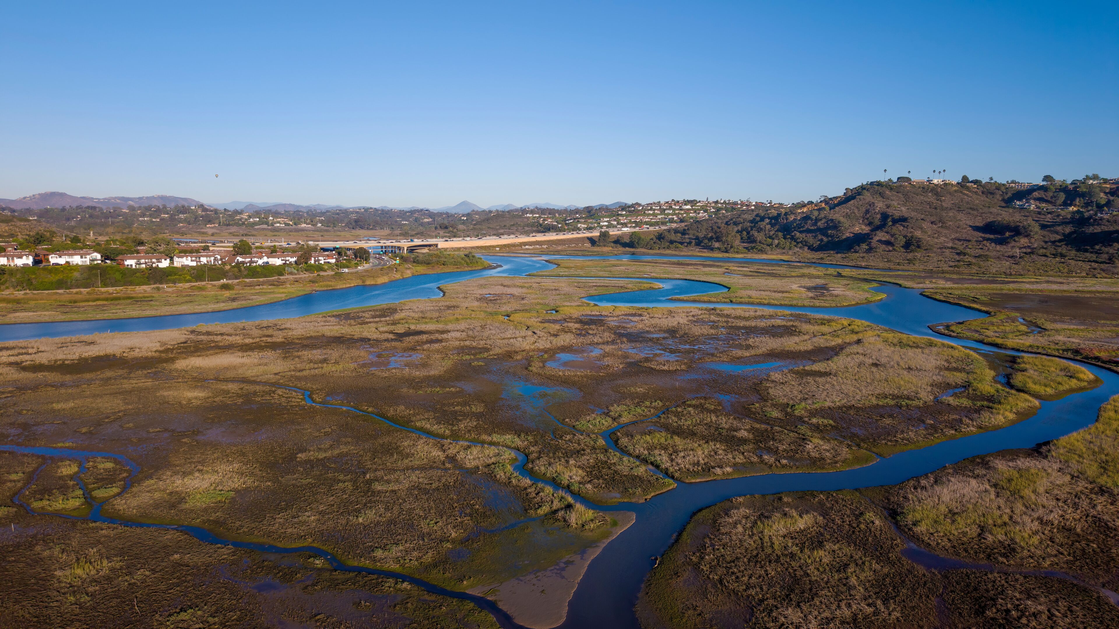 Un río serpenteando a través de un paisaje pantanoso con un pueblo al fondo.