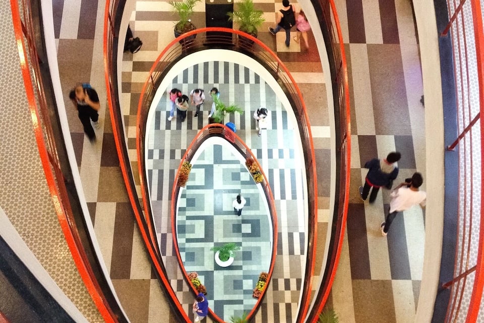A multi-level shopping mall with a central atrium featuring a geometric floor pattern and surrounding railings.