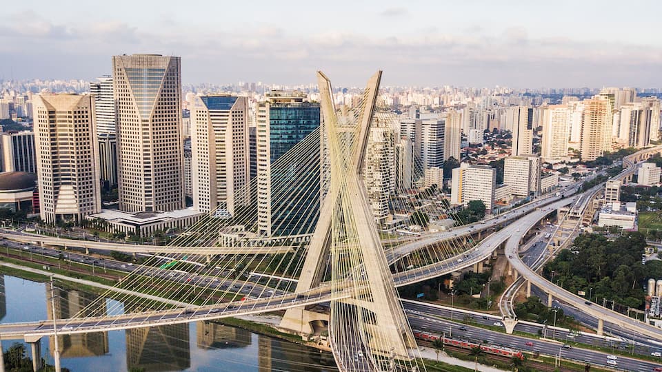 A cityscape with a prominent cable-stayed bridge, high-rise buildings, and a river reflecting the urban environment.