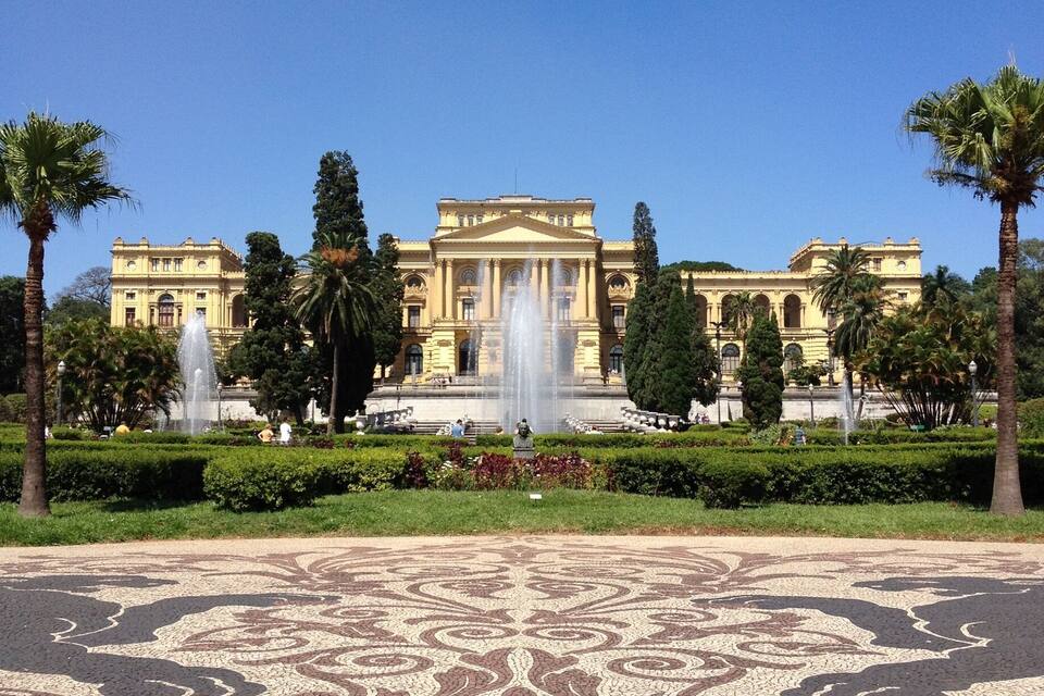 Un edificio imponente con una fuente central, rodeado de jardines cuidados y palmeras.