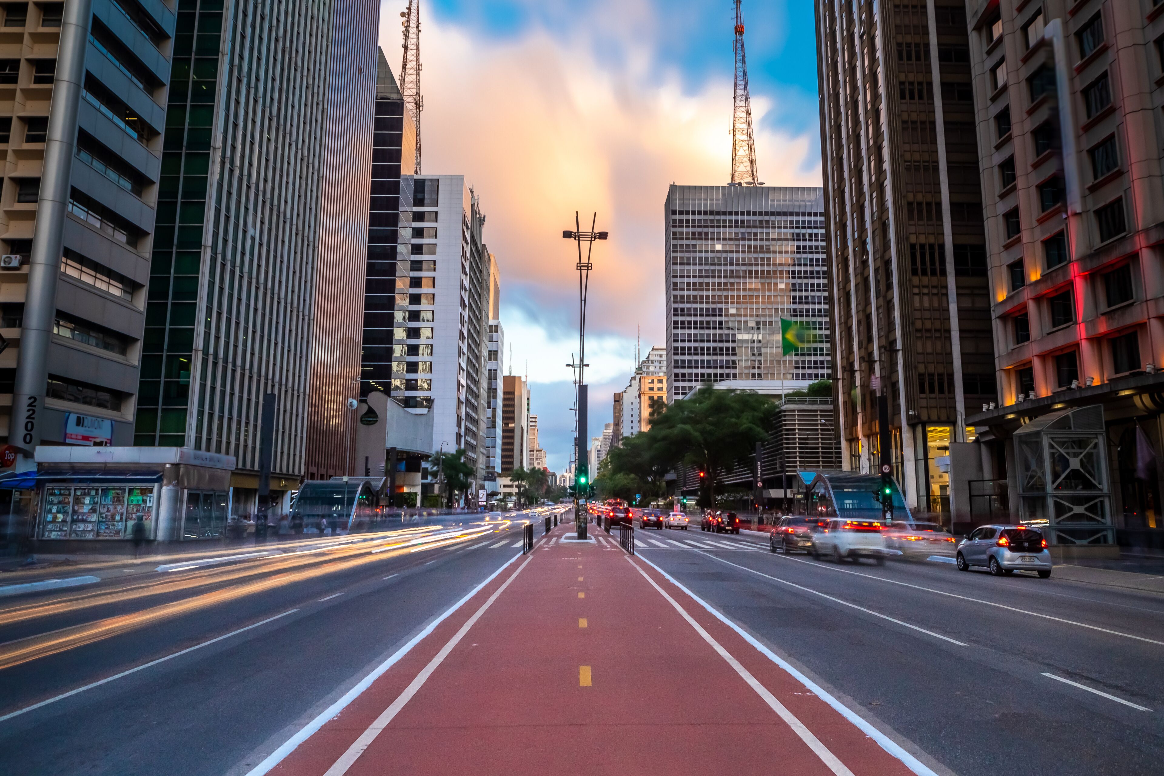Una calle urbana con edificios altos, un carril bici rojo y un semáforo verde.