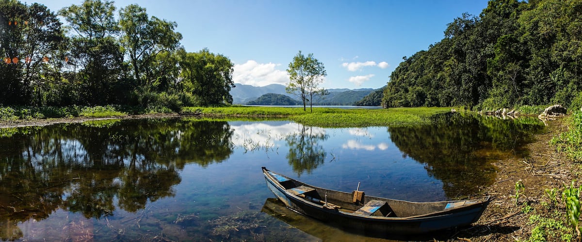 A calm river with a small boat, surrounded by lush greenery and distant mountains.