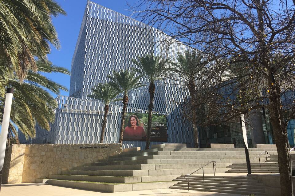 Un edificio moderno con una facciata geometrica, palme e una scala che conduce all'ingresso.