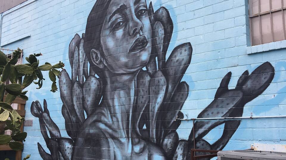 Ein Wandgemälde, das eine Hand zeigt, die sich nach vorne streckt, an einer blauen Wand.