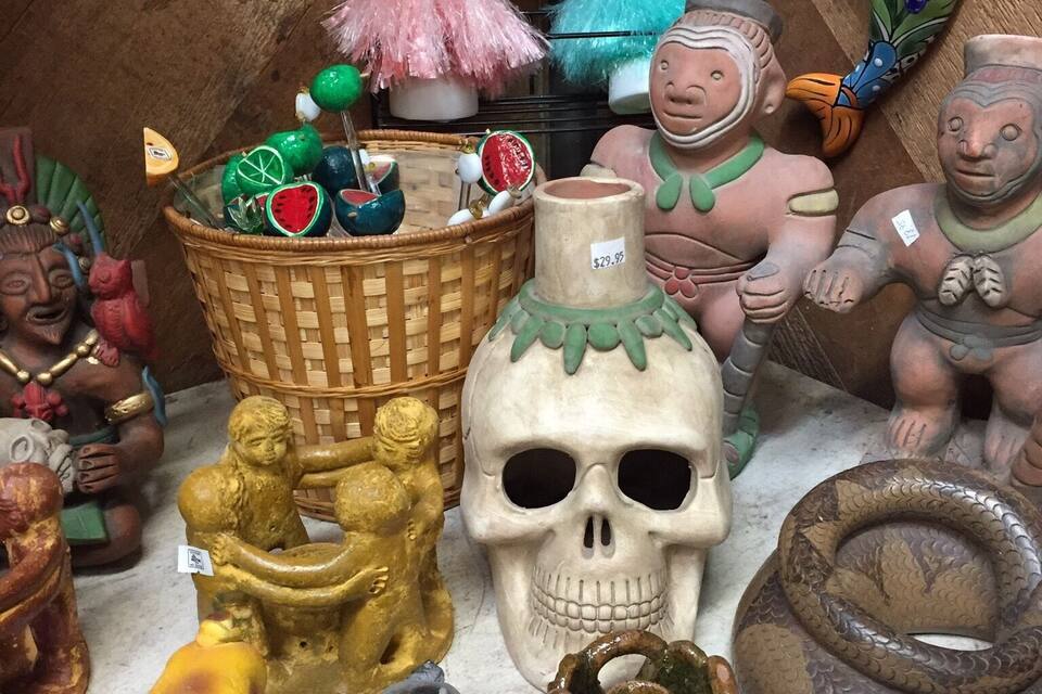 Diverse kleurrijke keramische beeldjes en sculpturen, waaronder een mand, een schedel en een pop in een roze jurk.