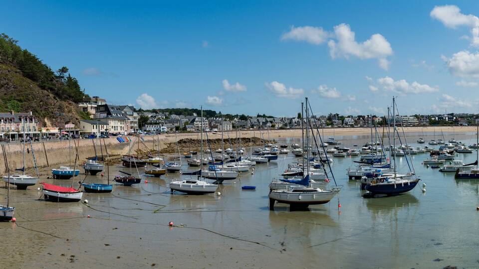 A coastal town with a beach, numerous boats, and buildings along the shore.