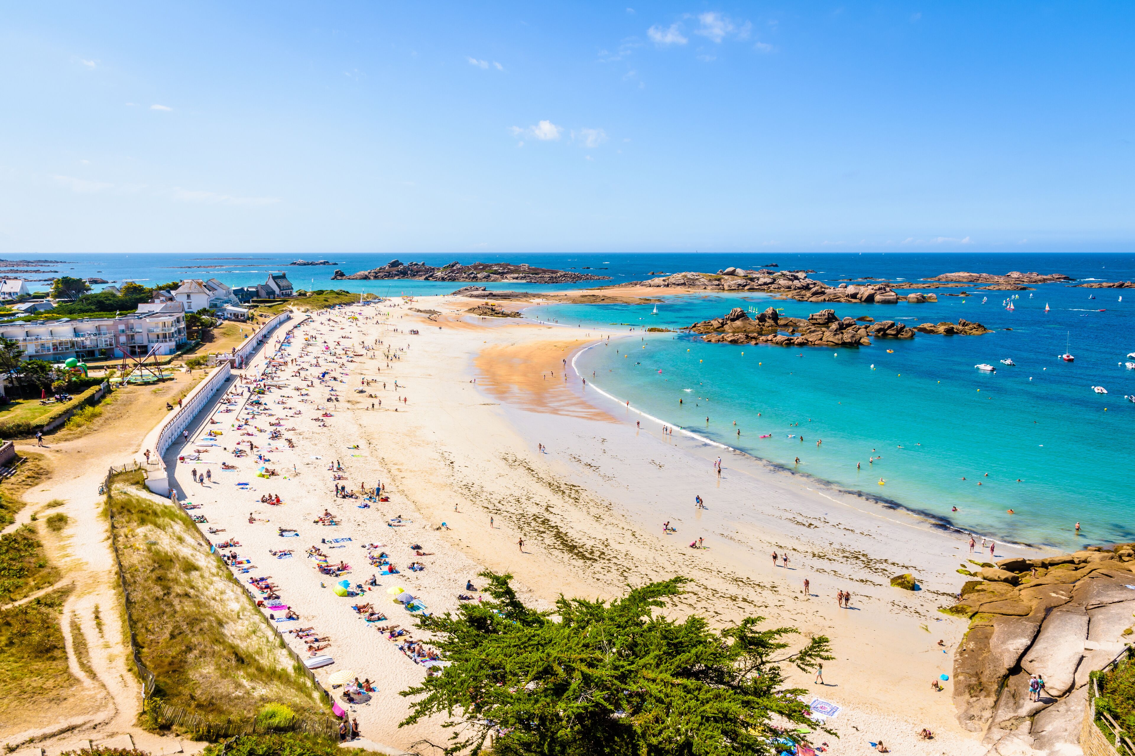 A coastal beach with clear turquoise waters, sandy shores, and rocky outcrops.