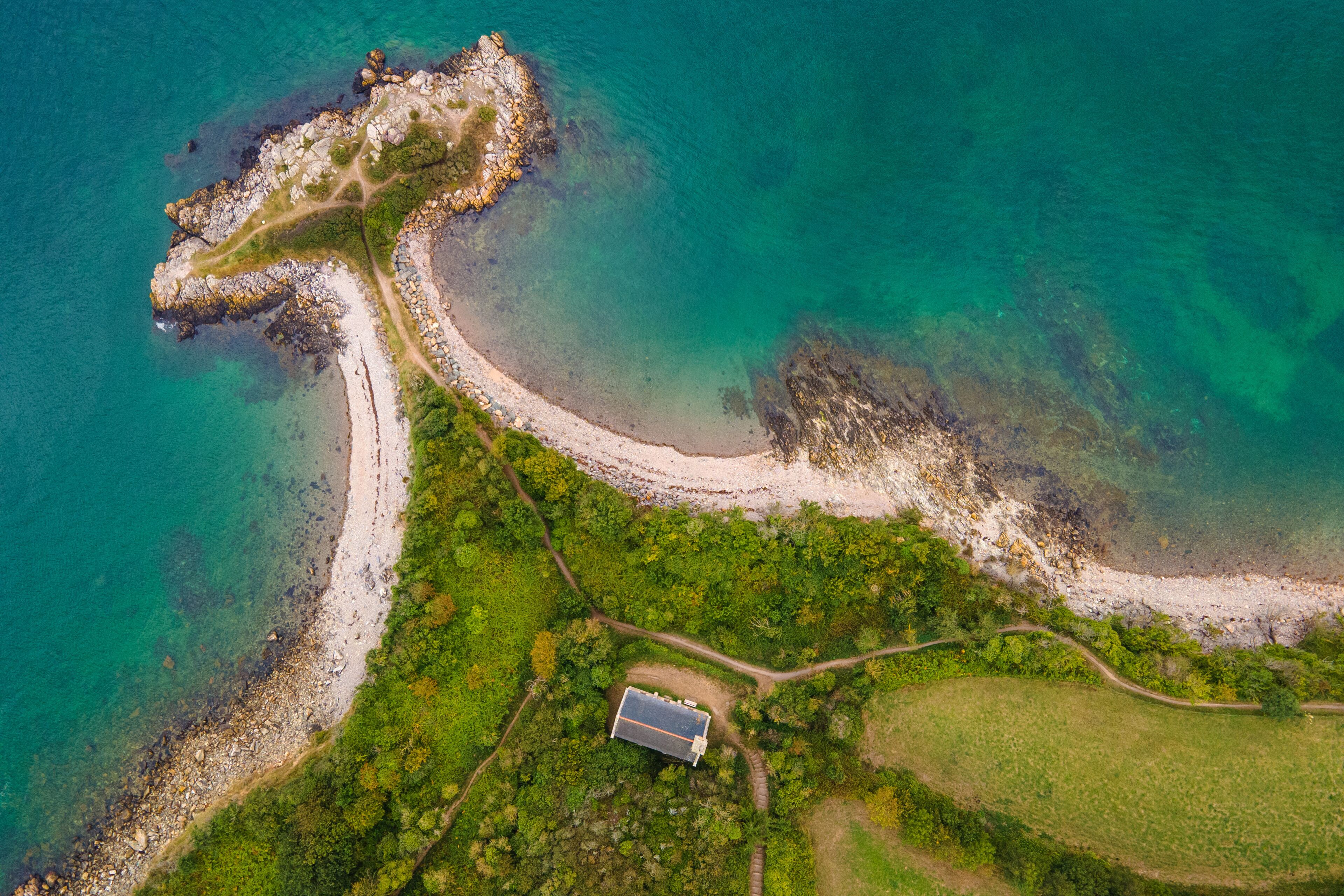 An aerial view of a coastal area with a rocky shoreline, a clear path leading to a building, and lush greenery.