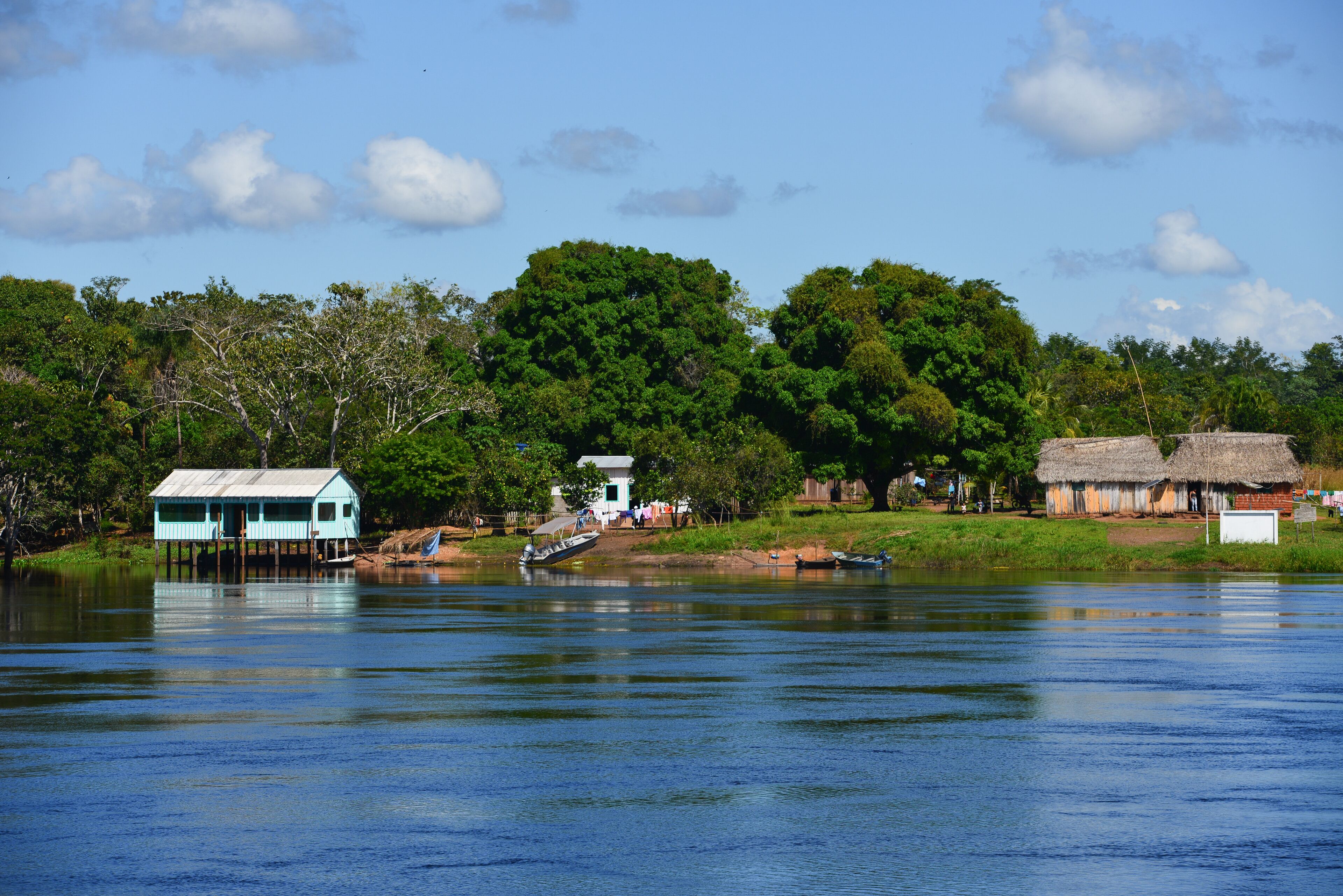 A calm river with houses on stilts, surrounded by lush greenery and trees.