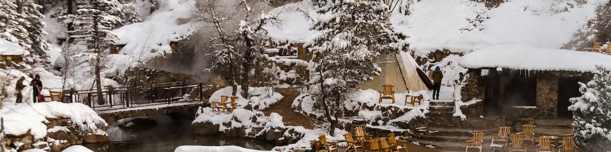 Un espace extérieur enneigé avec un pont en pierre, des chaises en bois et une source d’eau chaude.