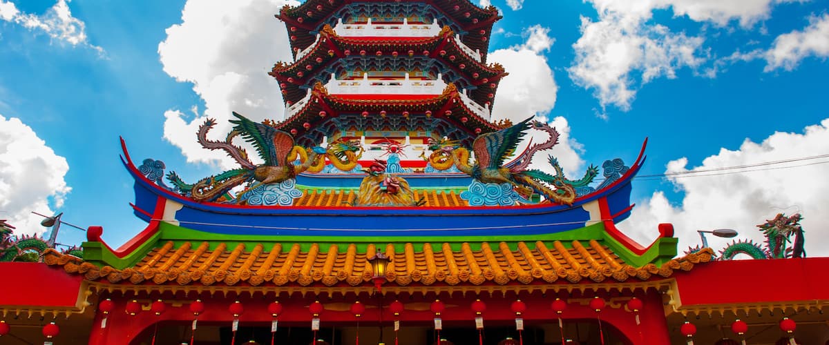 A multi-tiered pagoda with ornate decorations and red lanterns against a blue sky.