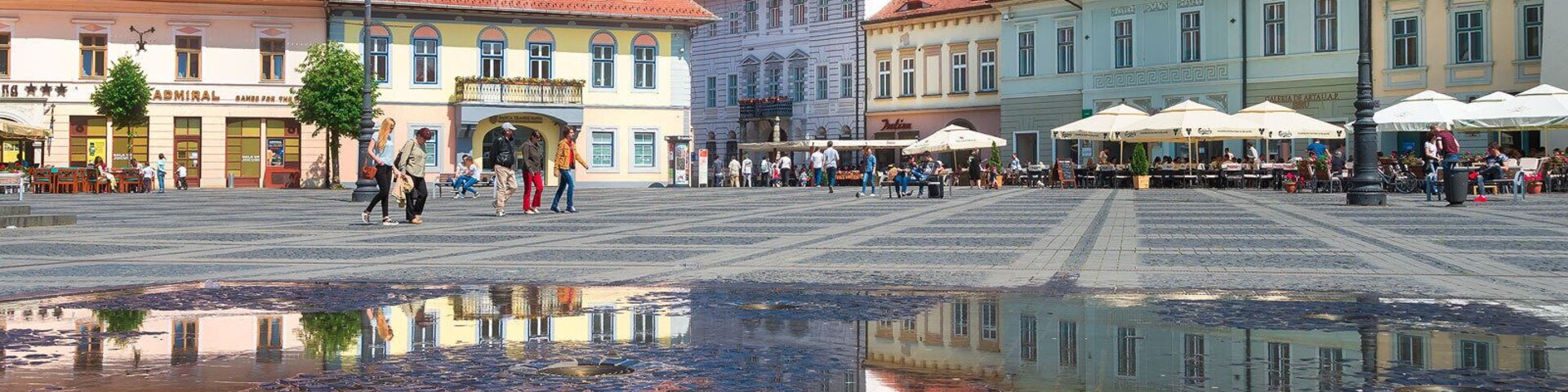 Uma praça histórica com calçamento de pedras, uma fonte central e arquitetura europeia tradicional.