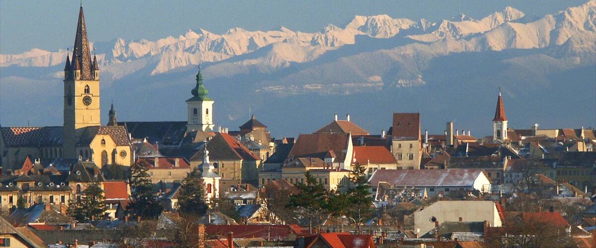 A town with a prominent church tower and snow-capped mountains in the background.
