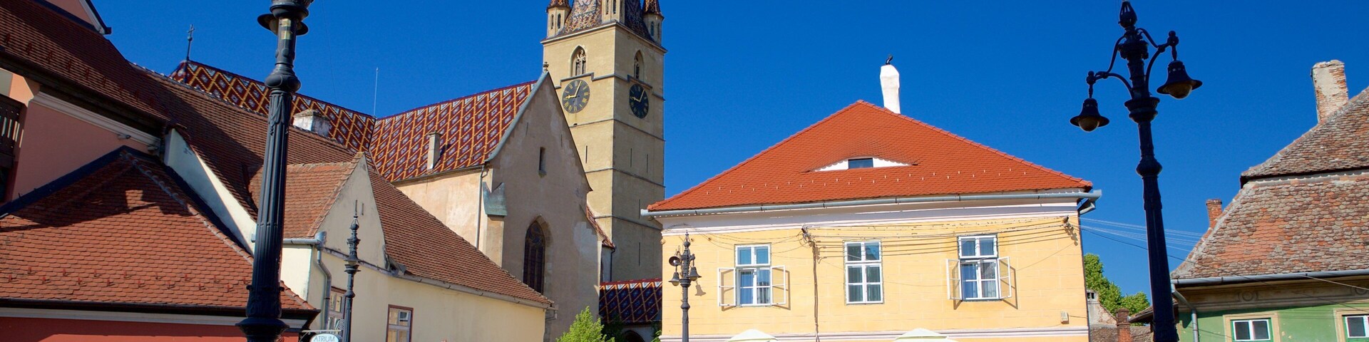 Uma praça histórica com uma igreja, um edifício amarelo e mesas ao ar livre.