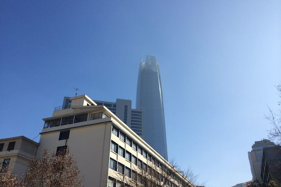 A tall skyscraper with a glass facade, surrounded by mid-rise buildings and bare trees.