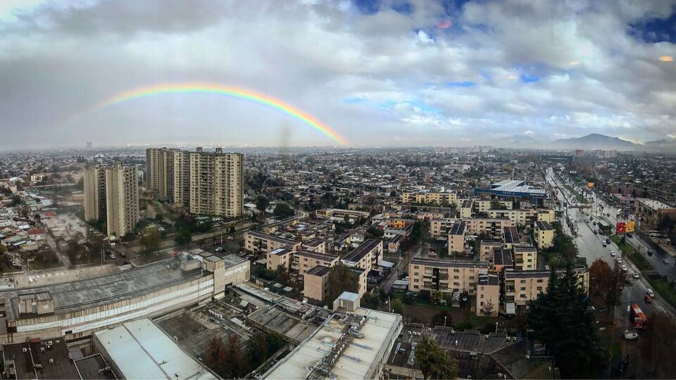 A cityscape with a rainbow over a cloudy sky.
