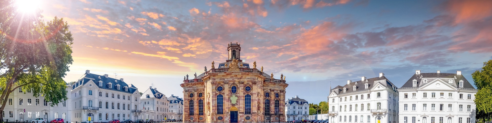 A historic building with ornate architecture, surrounded by white buildings and a cobblestone square.