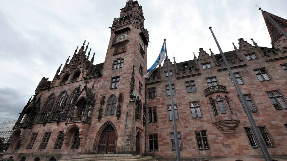 A historic building with intricate Gothic architecture, a prominent clock tower, and a flagpole with a flag.