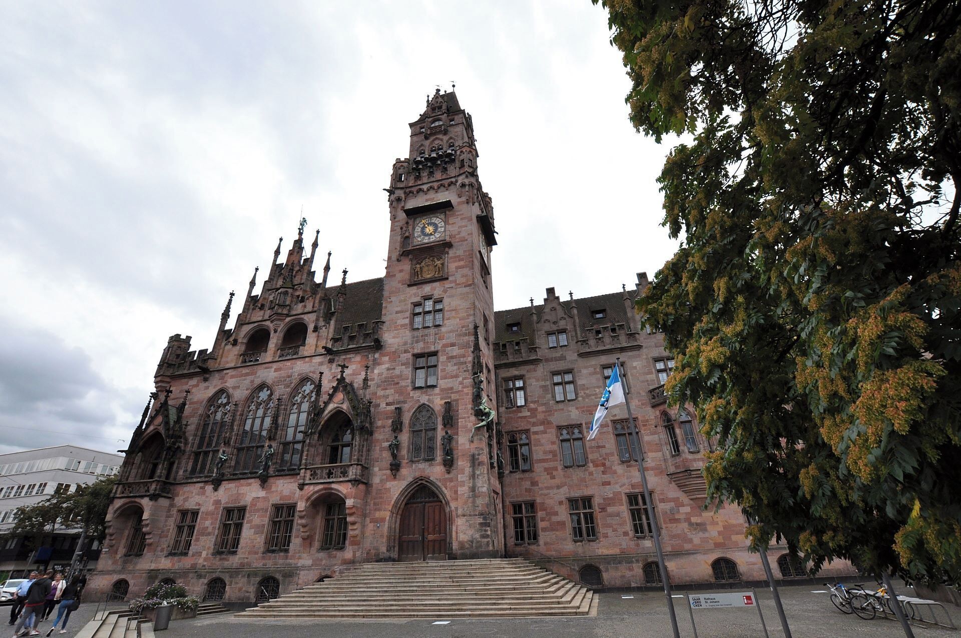 A historic building with intricate architecture, a prominent clock tower, and a flag.
