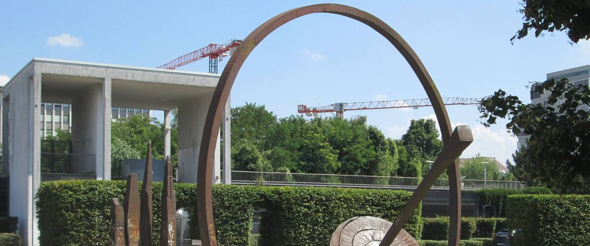 A sculpture with a circular element and a large arch in a grassy area.