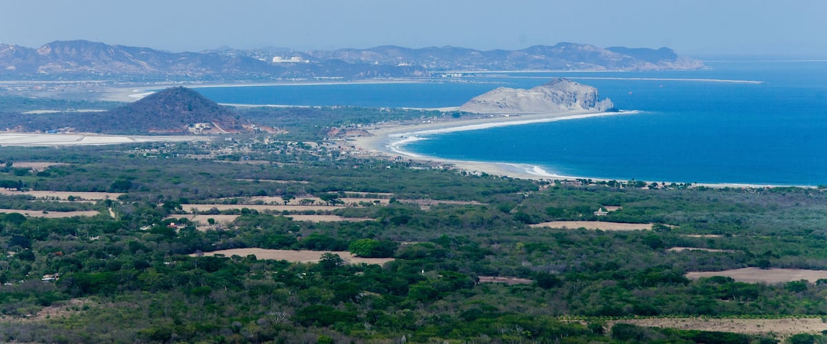 A coastal landscape with a prominent beach, a large hill, and distant mountains.