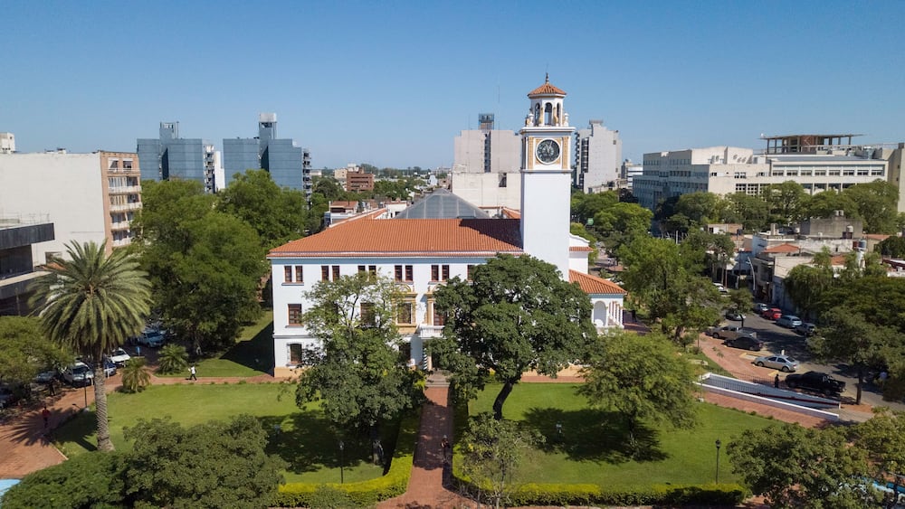 A historic building with a clock tower, surrounded by lush greenery and modern cityscape.