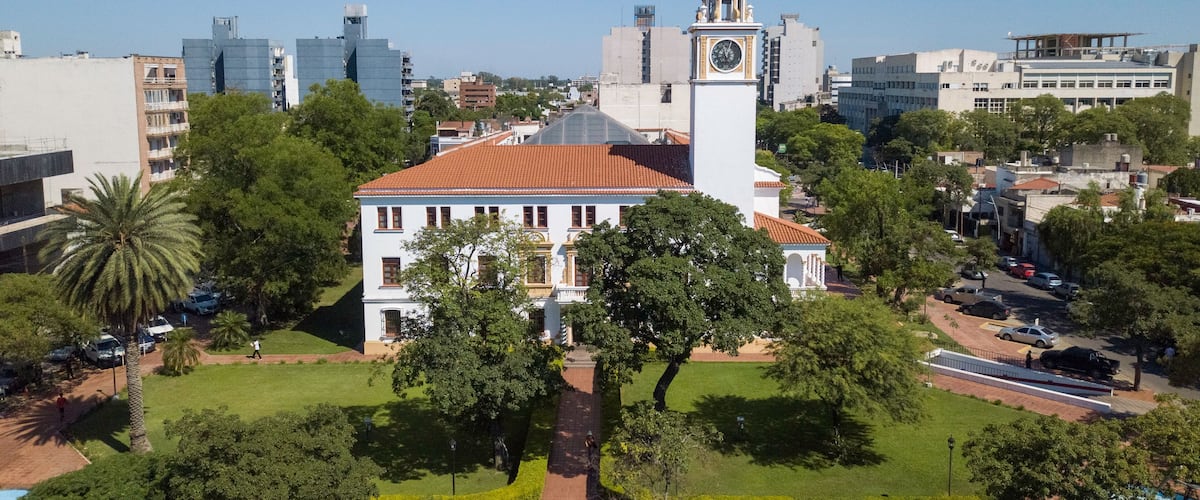 A historic building with a clock tower, surrounded by lush greenery and modern cityscape.