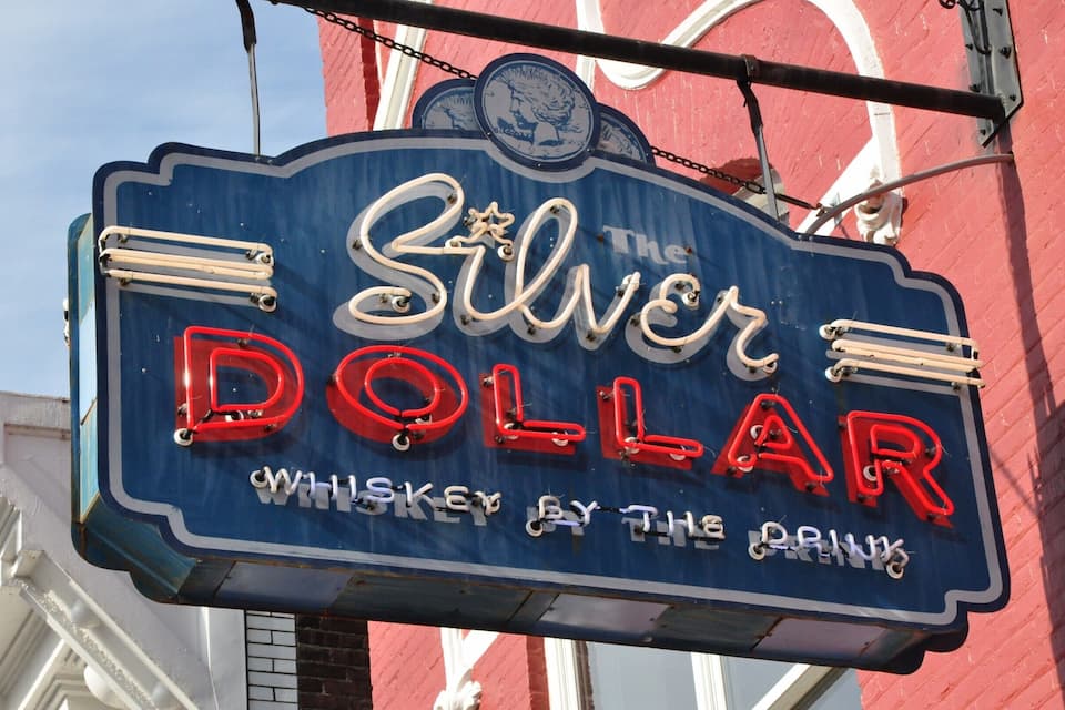 A neon sign for The Silver Dollar bar, featuring a whiskey theme.