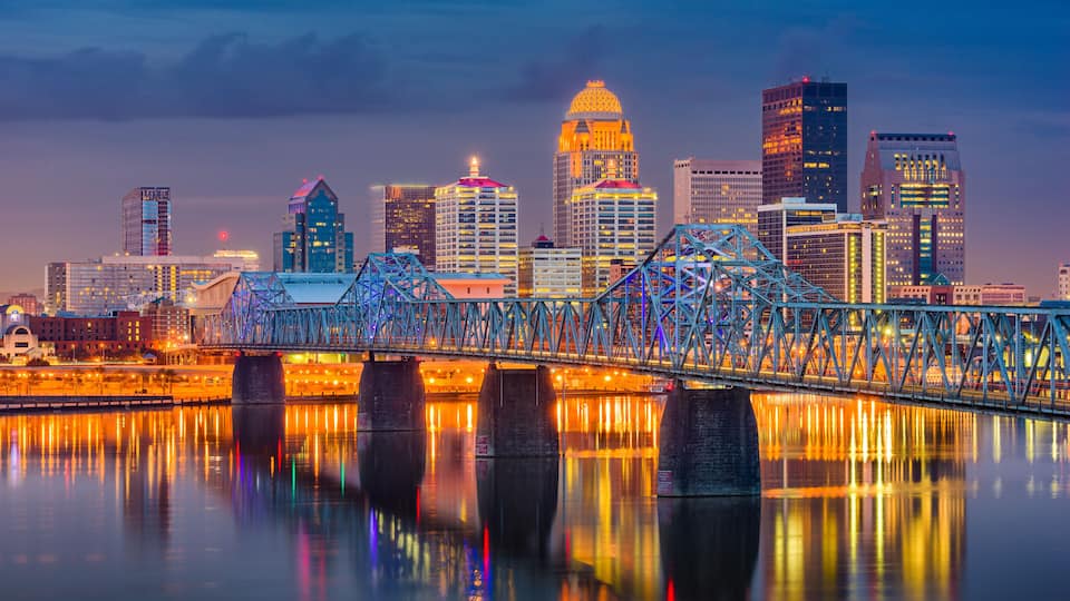 A city skyline with illuminated buildings, a prominent bridge, and a calm river reflecting the lights.