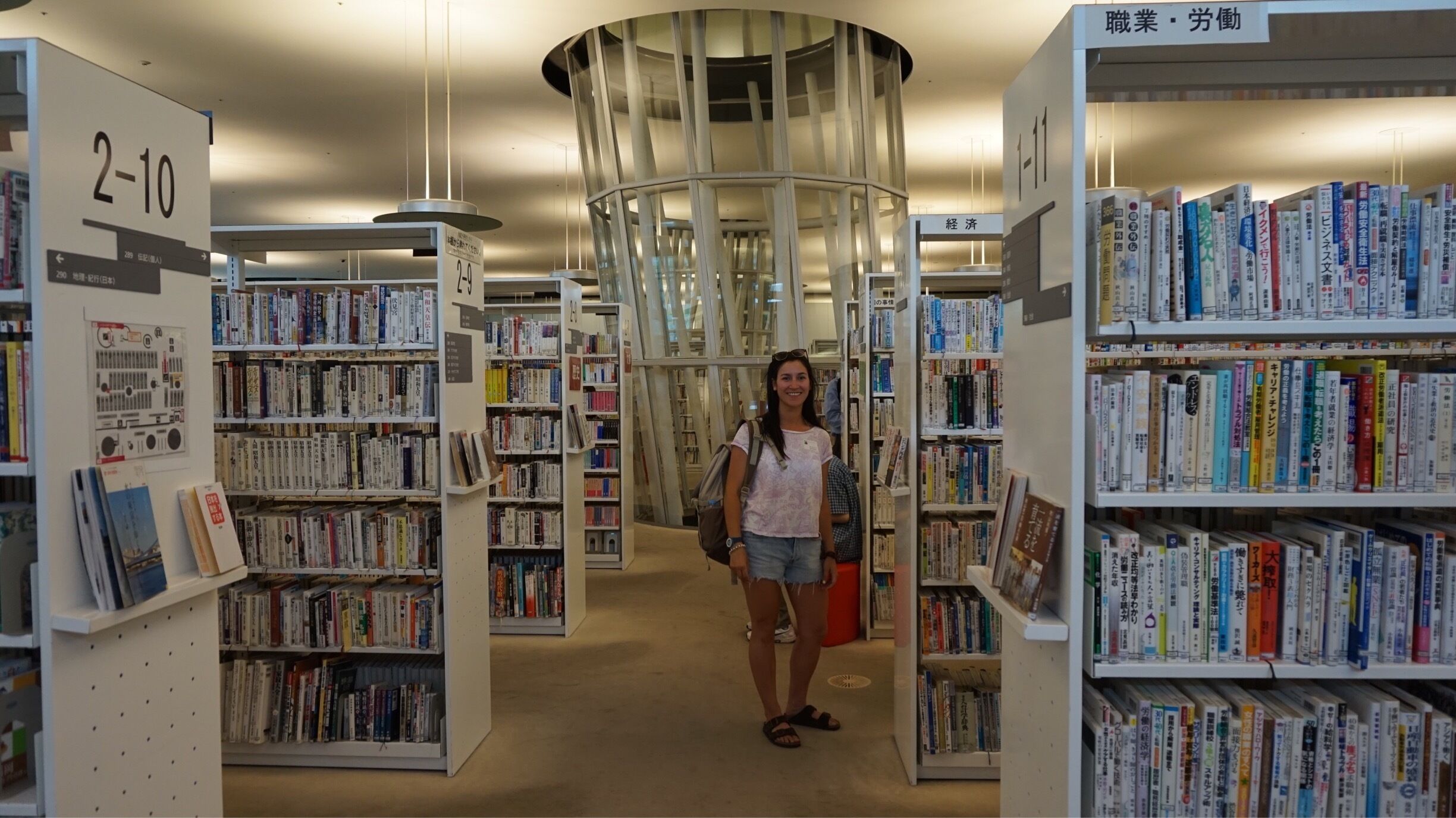 A library interior with bookshelves, a person, and a circular glass structure.