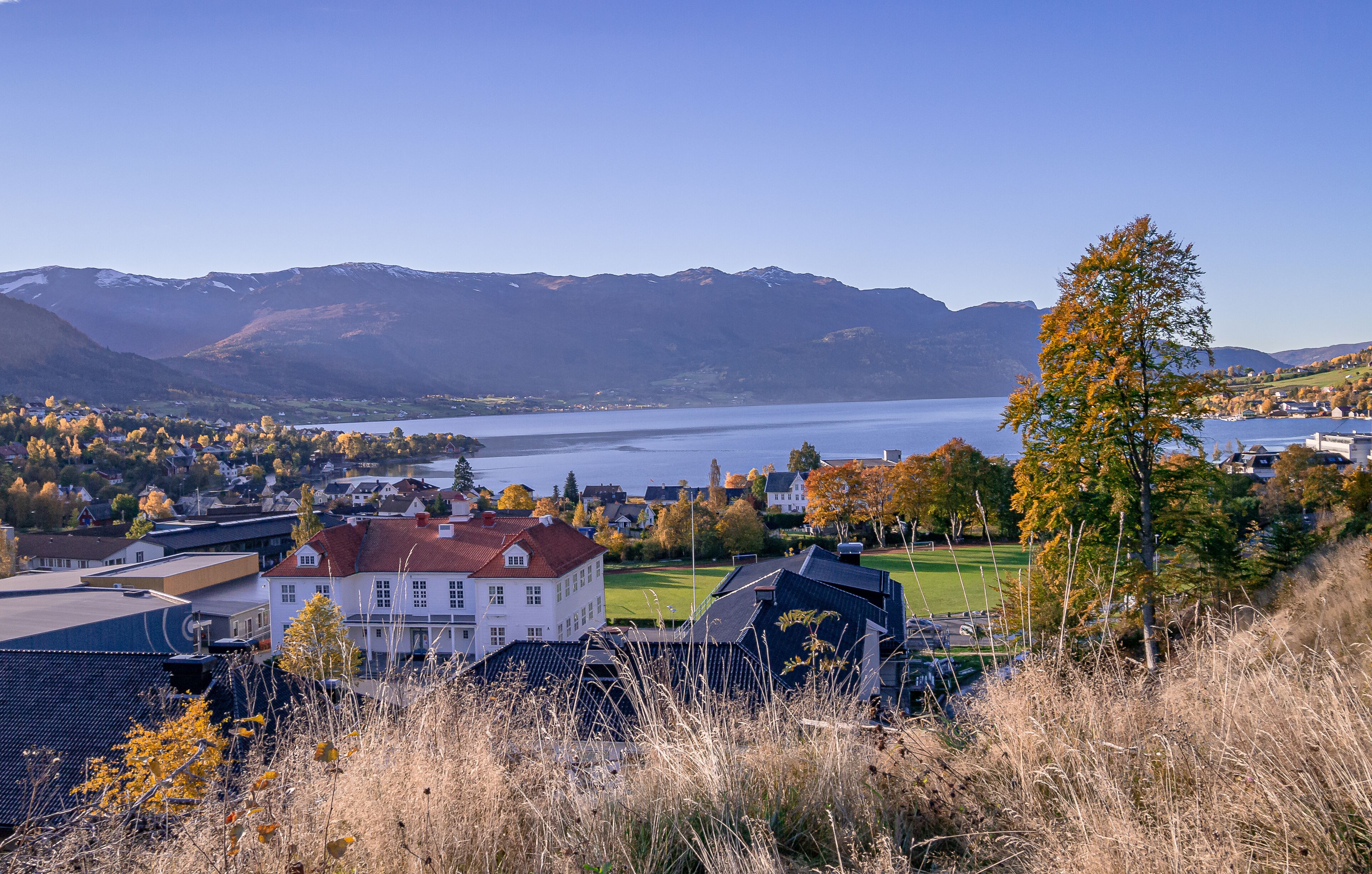 A lakeside town with mountains in the background, houses, and autumn foliage.