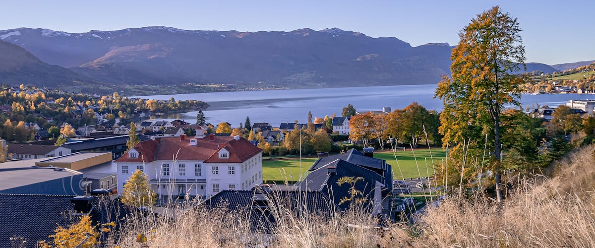A lakeside town with mountains in the background, houses, and autumn foliage.