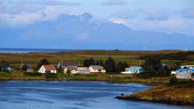 A coastal village with houses by the water, a lake, and mountains in the background.