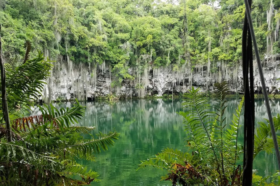 Um lago calmo rodeado por uma floresta densa e falésias de calcário.
