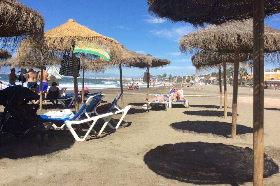 A beach with thatched umbrellas and lounge chairs.