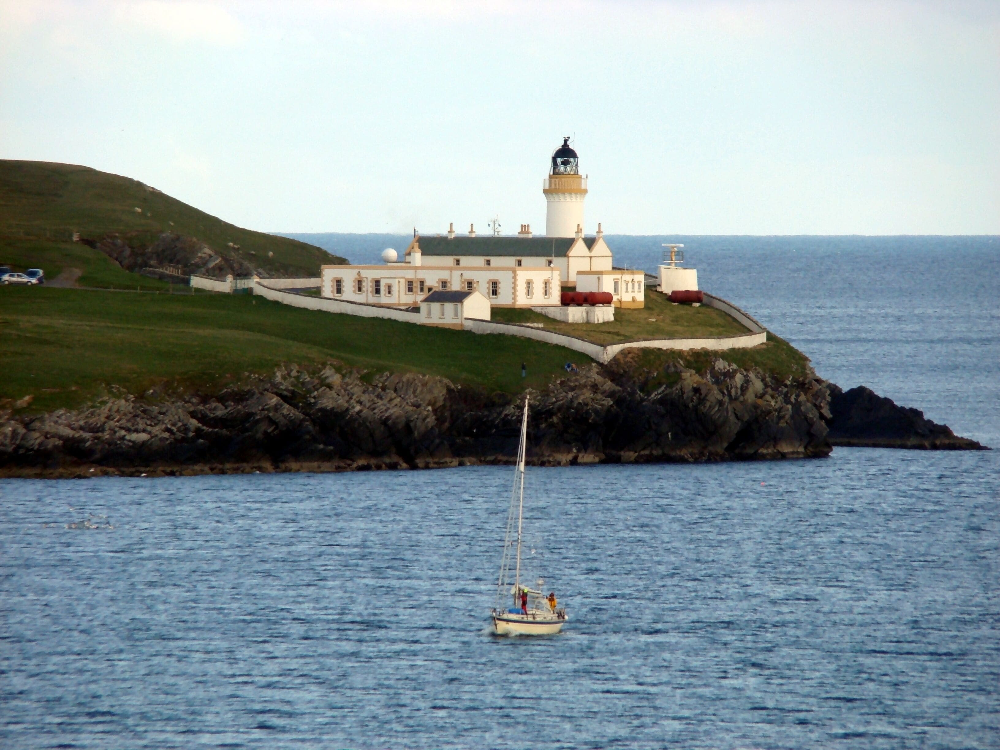 A lighthouse on a rocky island with a white building nearby.
